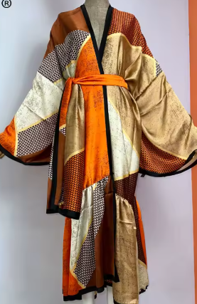 A patchwork kimono robe displayed on a mannequin, featuring large blocks of orange, beige, brown, and black patterned fabrics with a matching orange waist tie.